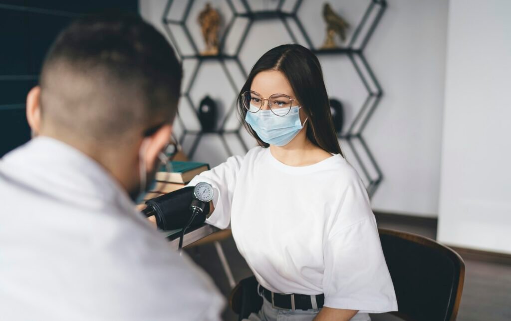 Woman in mask at doctors appointment measuring blood pressure